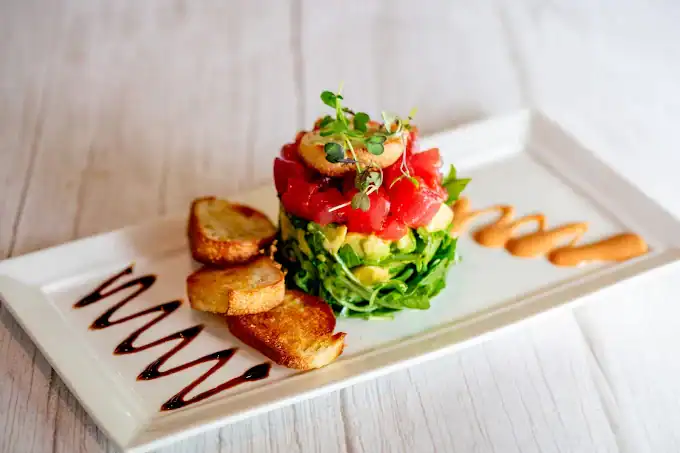 Fresh tartare with herbs, toasted garlic bread, and sauces on white plate.