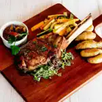 Juicy roasted lamb served with colorful grilled vegetables and crispy potatoes on a wooden platter.