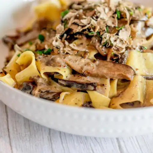 Rich pasta with mushrooms, truffle, and grated cheese, garnished with herbs.