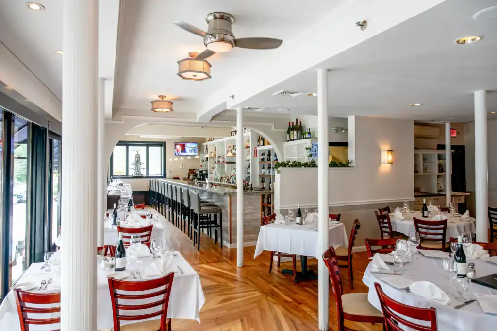 Modern restaurant decor featuring a bar, dining tables with white linens, and soft warm lighting.