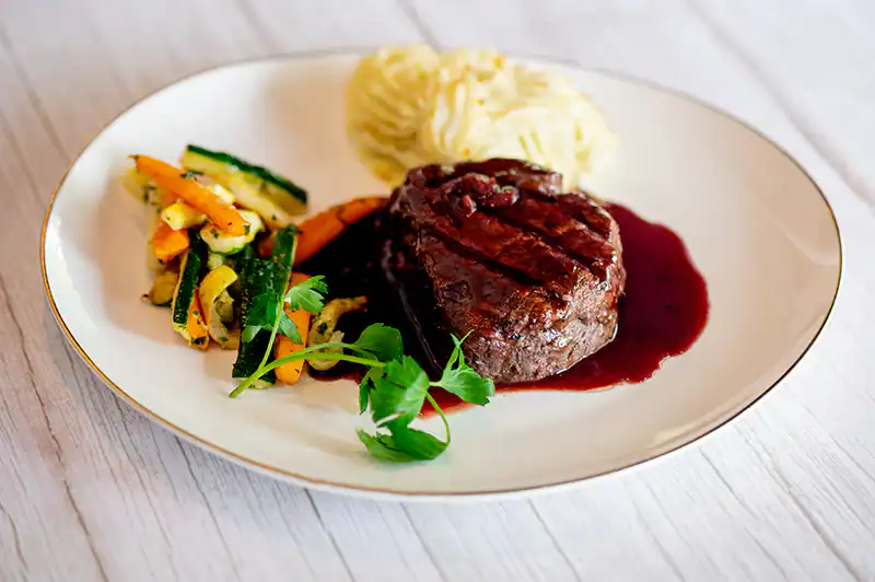 Delicious Tartufo steak with rich red wine sauce, mashed potatoes, and sautéed vegetables. Perfect gourmet meal presentation.