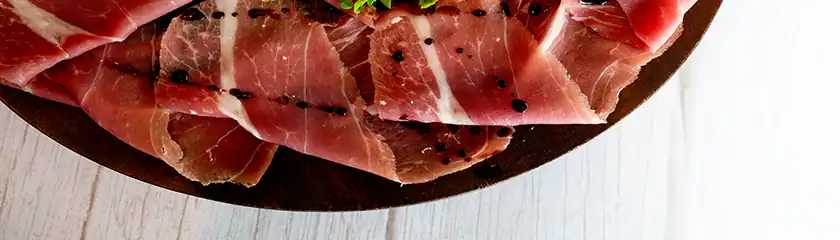 Premium cured ham with truffle flakes on a wooden plate, gourmet Italian delicacy.